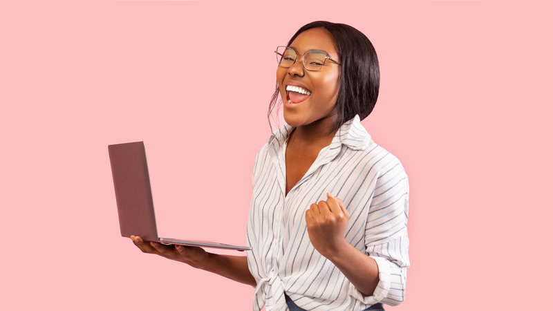 Happy woman working on a laptop in front of a pink backdrop