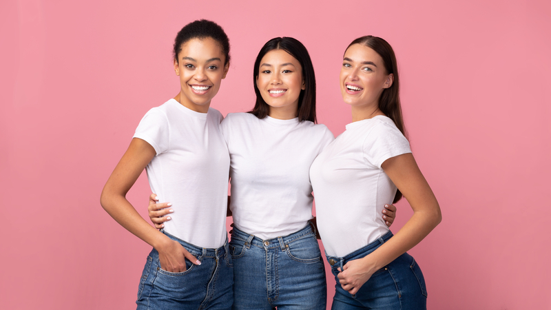 Three happy women in white tshirts posing in front of a pink background